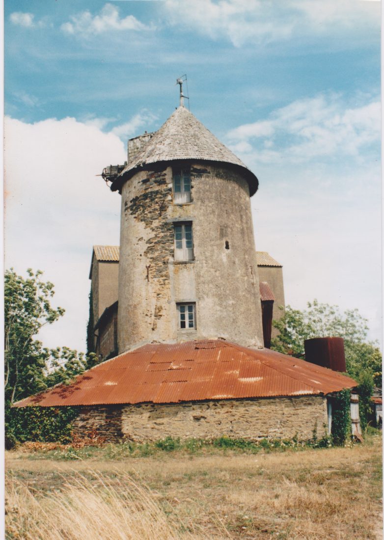 La tour du moulin avant restauration, coiffée de son ancienne toiture en bardeaux et flanquée d'un magasin au toit de tôle rouillée